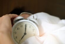 A close-up of a hand reaching for a ringing alarm clock, symbolizing waking up in the morning.
