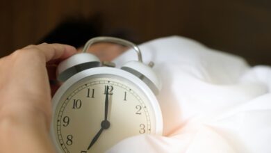 A close-up of a hand reaching for a ringing alarm clock, symbolizing waking up in the morning.