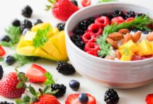 A vibrant bowl filled with fresh berries, mango, almonds, and herbs, perfect for a healthy snack or breakfast.