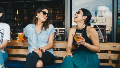 Two women laughing and enjoying drinks outdoors at a trendy bar, creating a vibrant and social atmosphere.