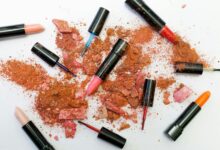 Colorful scattered makeup products including lipsticks and crushed powders on a white background.