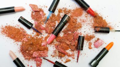 Colorful scattered makeup products including lipsticks and crushed powders on a white background.