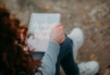 A woman holds a notebook with an inspirational quote, sitting outdoors.