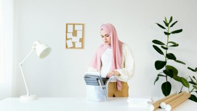 A woman wearing a hijab stands at a desk, organizing documents in a modern, minimalist office setting.